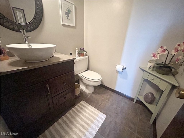 half bathroom with tile patterned floors, baseboards, toilet, and vanity