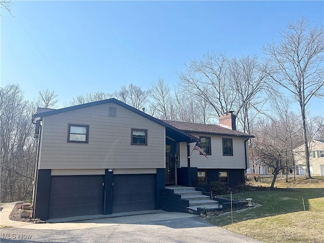 raised ranch with a chimney, driveway, a front yard, and a garage