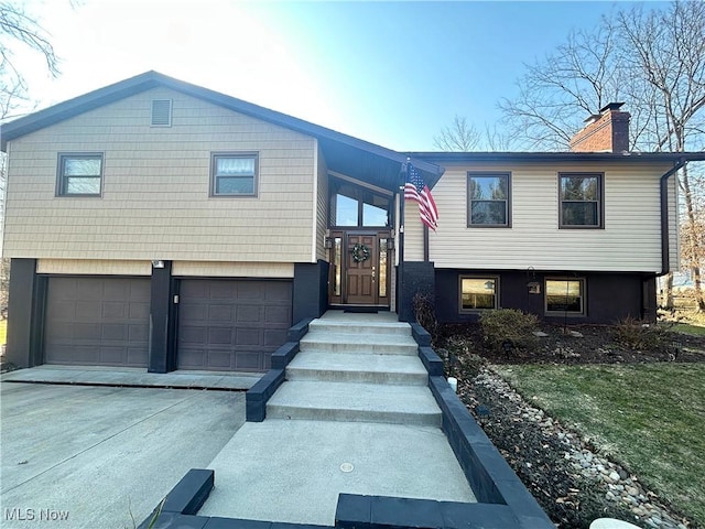 split foyer home featuring driveway, a chimney, and an attached garage