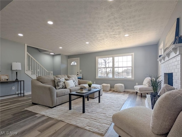 living room featuring a brick fireplace, baseboards, stairway, wood finished floors, and a textured ceiling