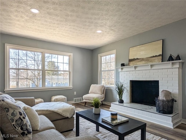 living room featuring wood finished floors, visible vents, baseboards, a textured ceiling, and a brick fireplace