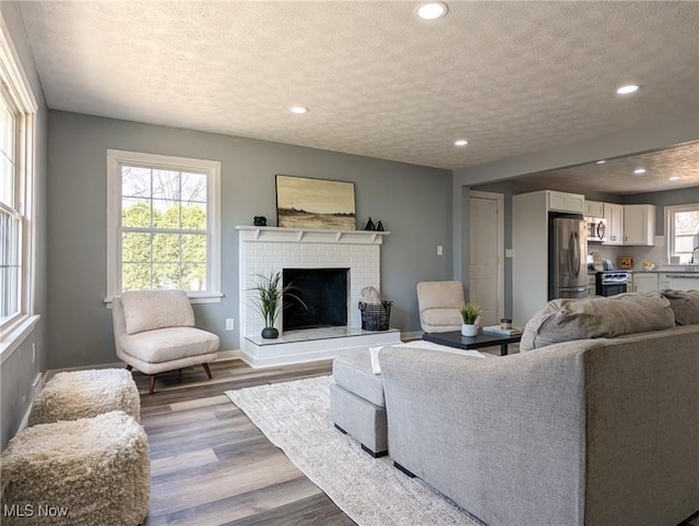 living room featuring a textured ceiling, wood finished floors, recessed lighting, a fireplace, and baseboards