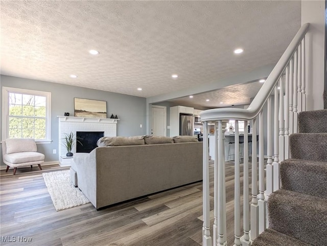 living area with a textured ceiling, wood finished floors, recessed lighting, stairway, and a fireplace