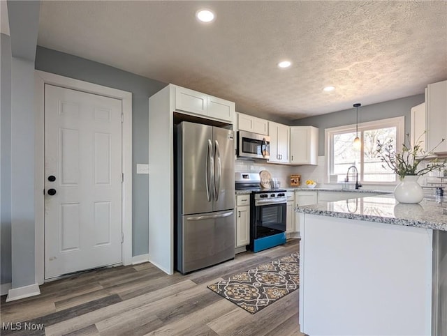 kitchen with white cabinets, light stone counters, light wood-style flooring, and stainless steel appliances