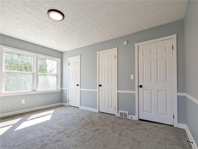 unfurnished bedroom with carpet, visible vents, baseboards, a textured ceiling, and two closets