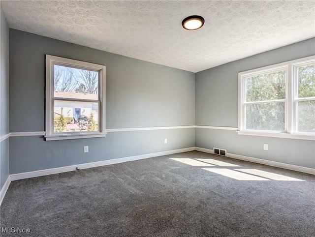 carpeted empty room with visible vents, a healthy amount of sunlight, a textured ceiling, and baseboards