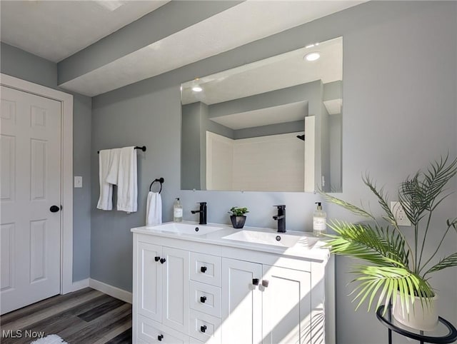 full bathroom featuring double vanity, wood finished floors, baseboards, and a sink