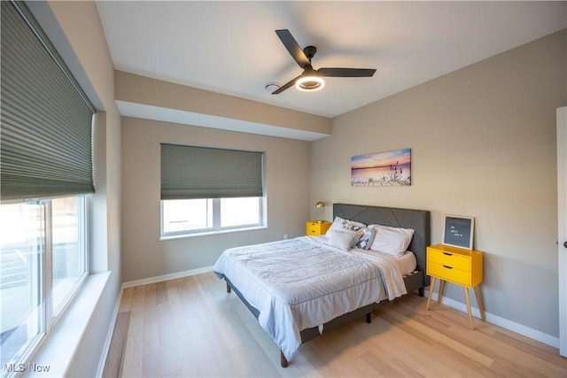 bedroom featuring a ceiling fan, multiple windows, wood finished floors, and baseboards