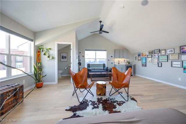 living room featuring a ceiling fan, light wood-type flooring, baseboards, and vaulted ceiling