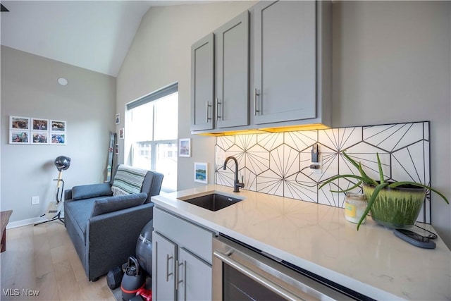 kitchen with gray cabinetry, a sink, tasteful backsplash, light wood-style floors, and vaulted ceiling