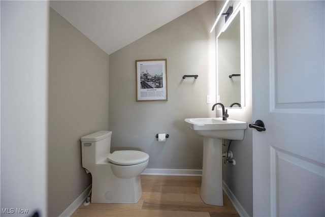 half bathroom with toilet, a sink, wood finished floors, baseboards, and vaulted ceiling