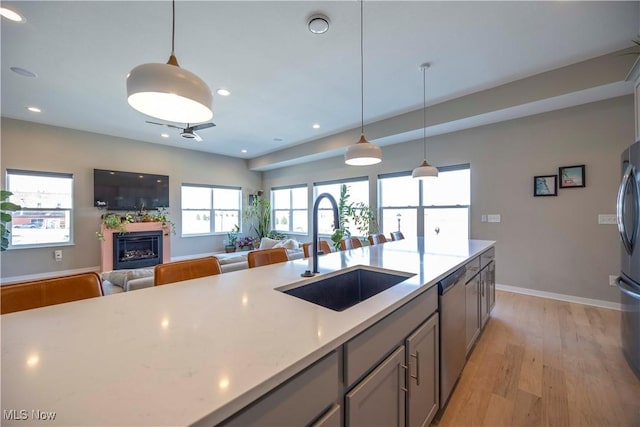 kitchen with open floor plan, light wood-style flooring, appliances with stainless steel finishes, a fireplace, and a sink