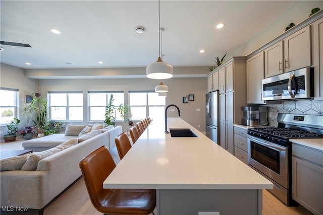 kitchen with gray cabinetry, open floor plan, light countertops, stainless steel appliances, and a sink