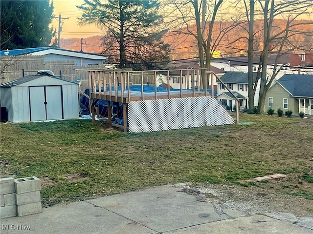 yard at dusk featuring a swimming pool, fence, a shed, a residential view, and an outdoor structure