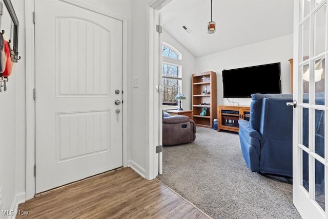 carpeted foyer with vaulted ceiling, wood finished floors, and visible vents