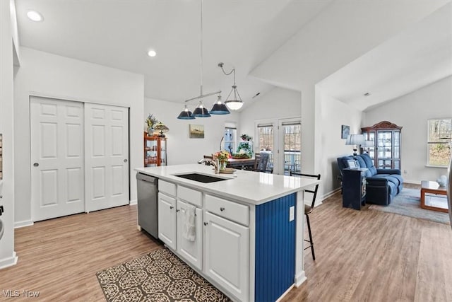 kitchen with a sink, vaulted ceiling, open floor plan, stainless steel dishwasher, and light wood-type flooring