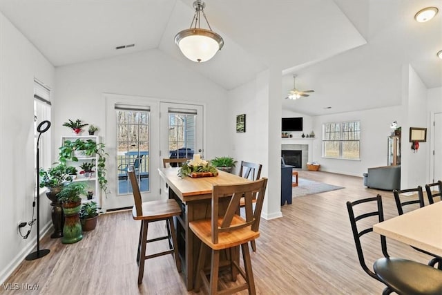 dining room featuring visible vents, wood finished floors, a tiled fireplace, and vaulted ceiling