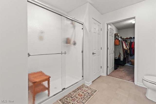 full bathroom with a walk in closet, a shower stall, toilet, and baseboards