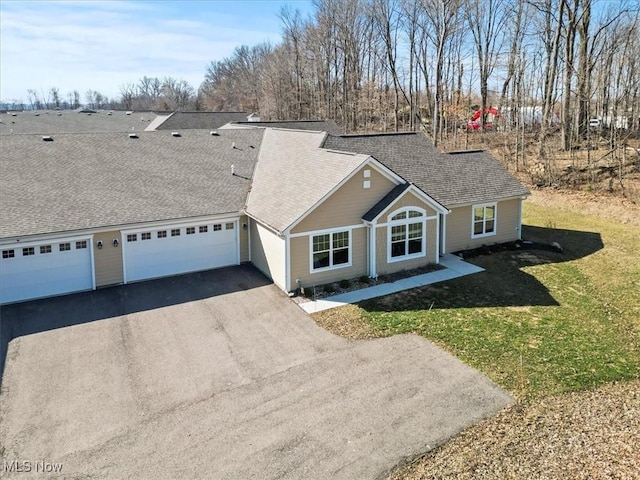 view of front of property with aphalt driveway, a garage, roof with shingles, and a front yard