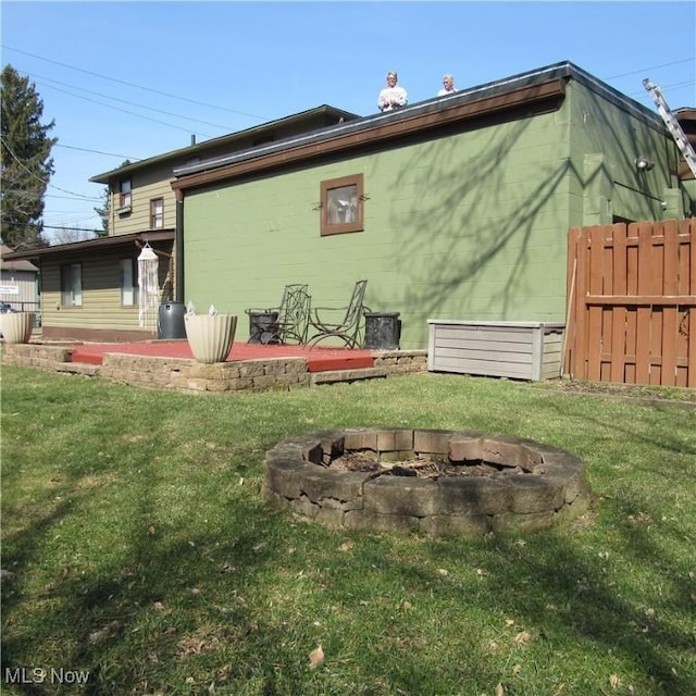 rear view of house with a lawn, concrete block siding, an outdoor fire pit, and fence