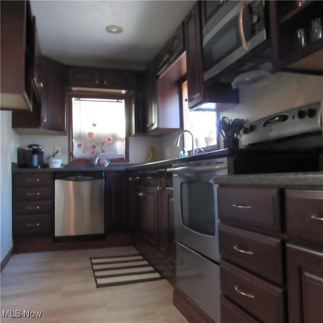 kitchen featuring light wood-type flooring, a sink, dark countertops, appliances with stainless steel finishes, and washer / dryer