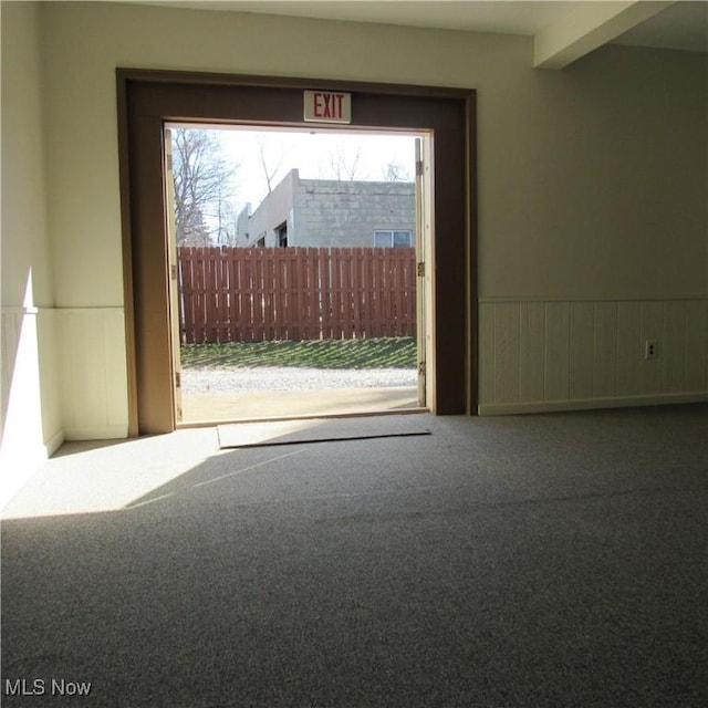 carpeted spare room featuring beamed ceiling, plenty of natural light, and wainscoting