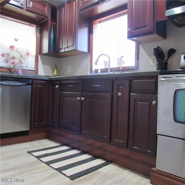 kitchen with dark countertops, ventilation hood, stainless steel dishwasher, wood finished floors, and a sink