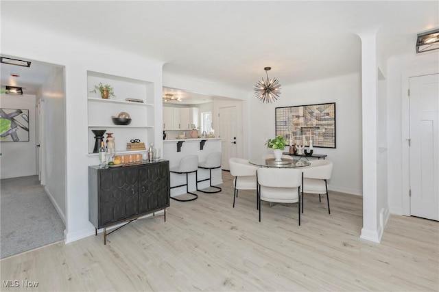 dining room featuring an inviting chandelier, built in shelves, baseboards, and light wood-type flooring