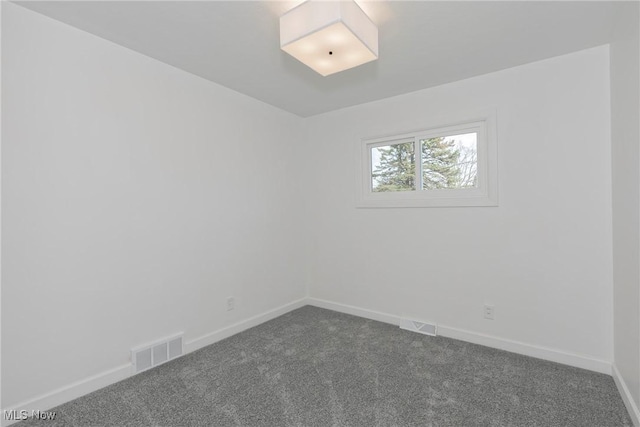 spare room featuring visible vents, baseboards, and dark colored carpet