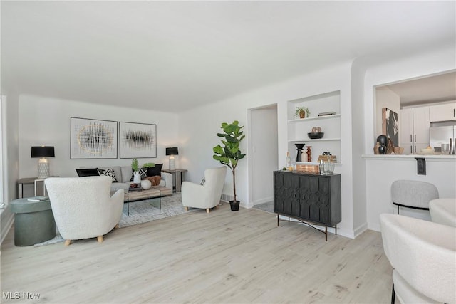 living area with built in shelves, baseboards, and light wood-style floors