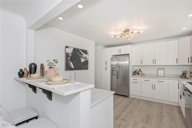 kitchen with a kitchen bar, light wood-style flooring, white cabinets, and stainless steel appliances