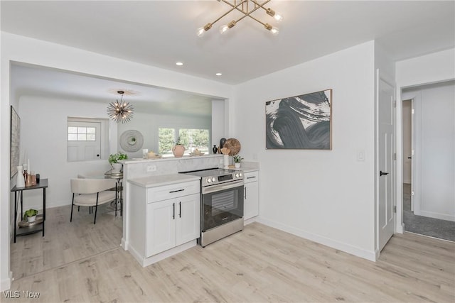 kitchen featuring stainless steel electric range oven, an inviting chandelier, a peninsula, light countertops, and white cabinets