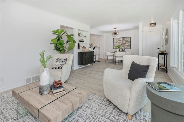 living area with built in shelves, baseboards, visible vents, and light wood-type flooring