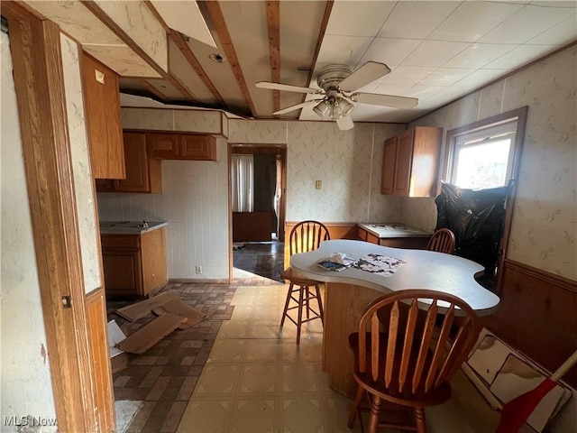 dining space with wallpapered walls, tile patterned floors, a ceiling fan, and wainscoting