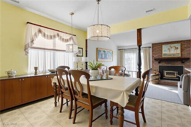 dining space with a brick fireplace, beamed ceiling, light tile patterned floors, and visible vents