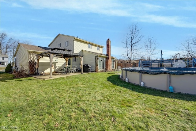 rear view of property with a covered pool, a gazebo, a yard, and a patio