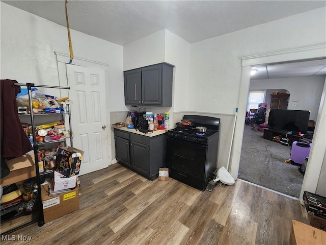 kitchen with black gas range oven, gray cabinets, light countertops, and wood finished floors