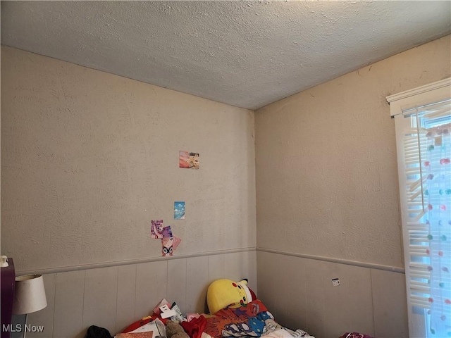 unfurnished bedroom with a textured ceiling, a textured wall, and wainscoting