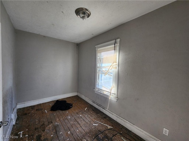 empty room featuring baseboards, wood-type flooring, and a textured ceiling