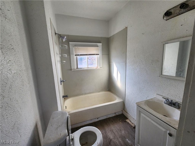 full bathroom with vanity, wood finished floors, tub / shower combination, toilet, and a textured wall