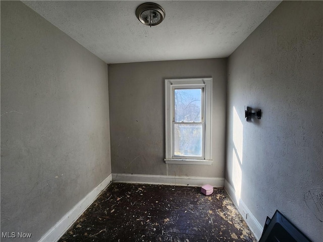 empty room with a textured wall, baseboards, and a textured ceiling