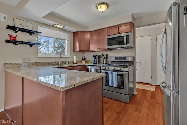 kitchen featuring brown cabinets, light wood-style flooring, a sink, appliances with stainless steel finishes, and a peninsula