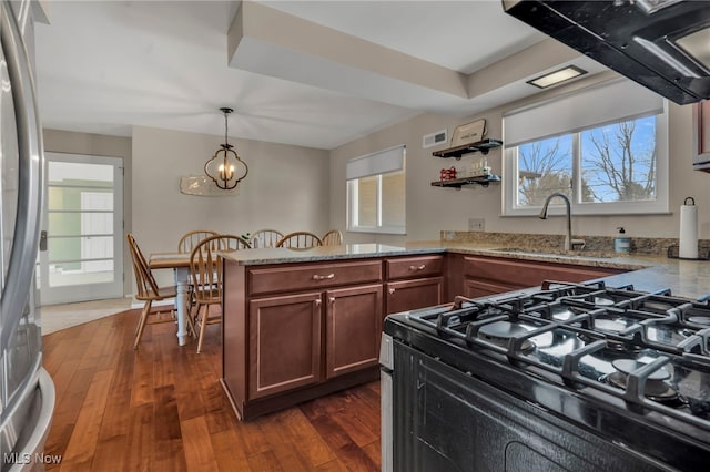 kitchen featuring a peninsula, dark wood-style flooring, a sink, stainless steel refrigerator, and gas range