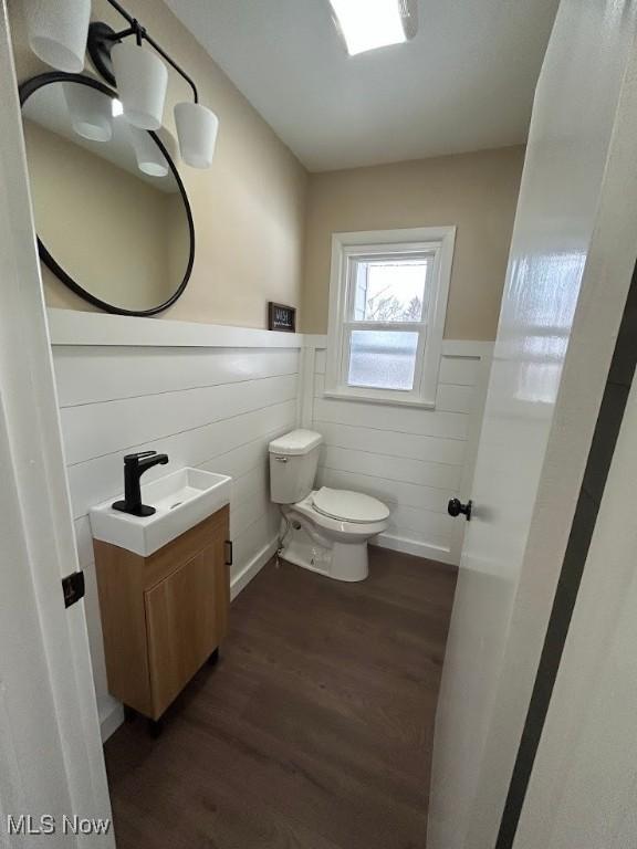 half bathroom featuring vanity, toilet, wood finished floors, and wainscoting