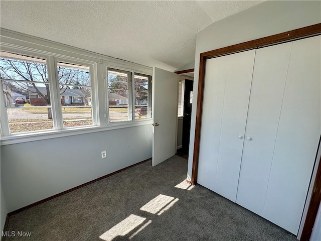 unfurnished bedroom featuring a textured ceiling, dark carpet, a closet, baseboards, and lofted ceiling