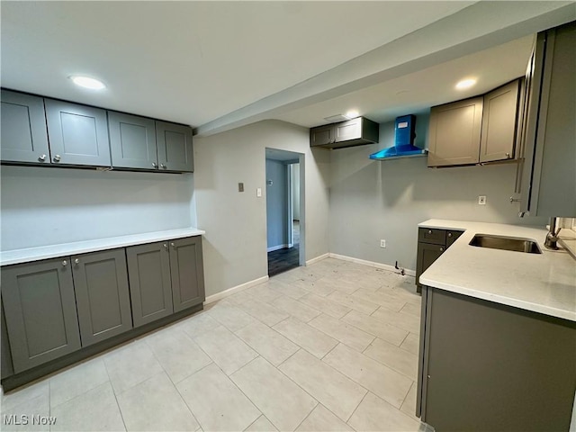 kitchen featuring gray cabinets, a sink, wall chimney range hood, light countertops, and baseboards