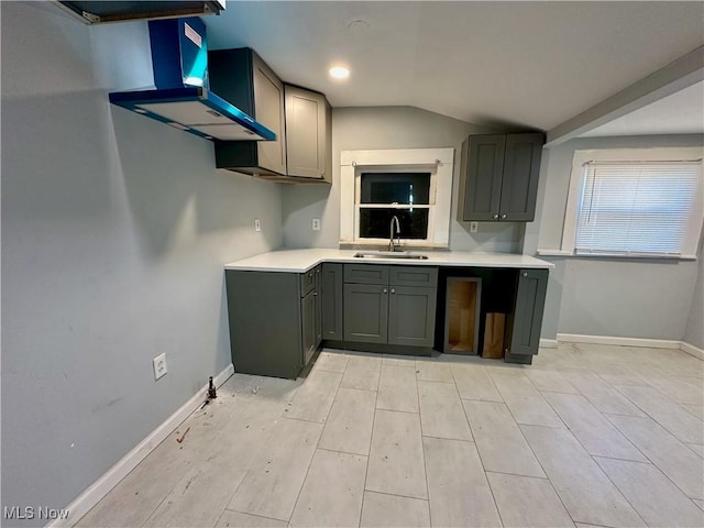 kitchen featuring baseboards, light countertops, lofted ceiling, gray cabinets, and a sink