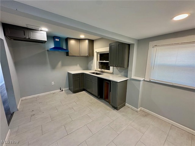 kitchen featuring baseboards, light countertops, wall chimney range hood, and a sink