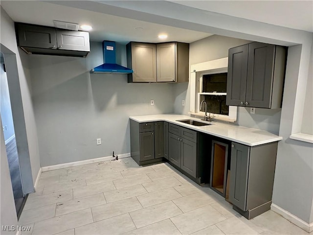 kitchen with gray cabinetry, wall chimney exhaust hood, baseboards, and a sink