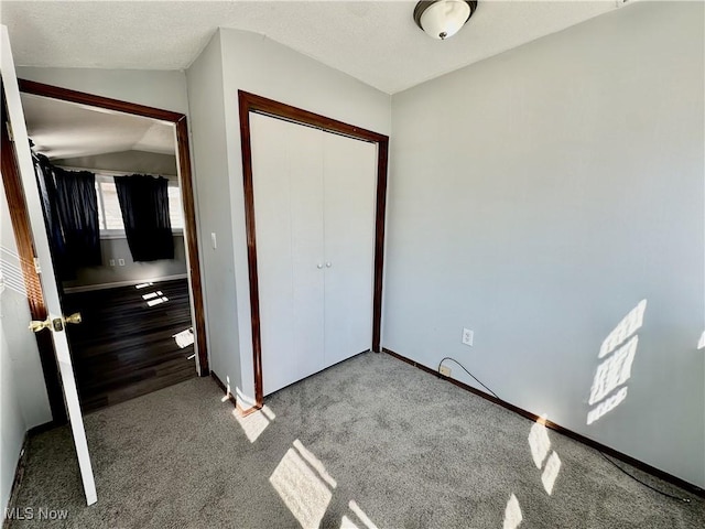 unfurnished bedroom featuring baseboards, carpet, vaulted ceiling, a closet, and a textured ceiling